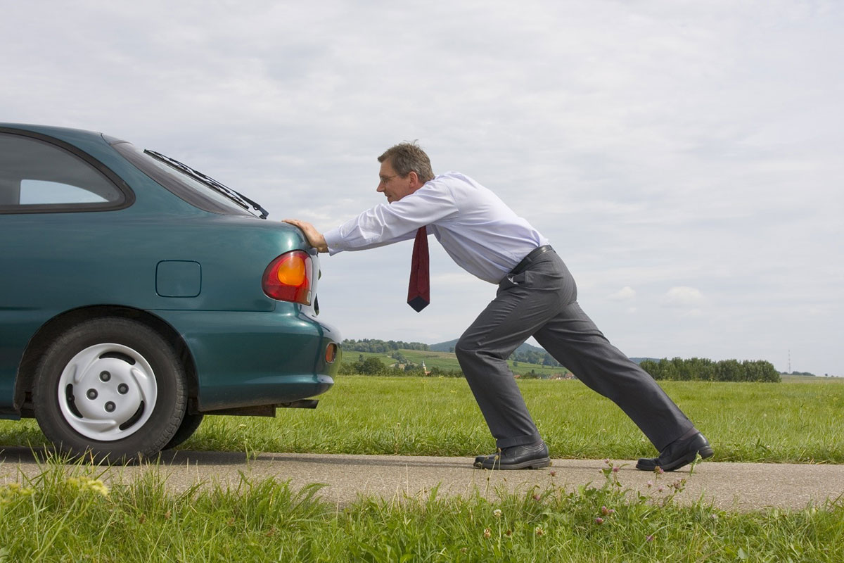 A businessman pushing his car down a road.